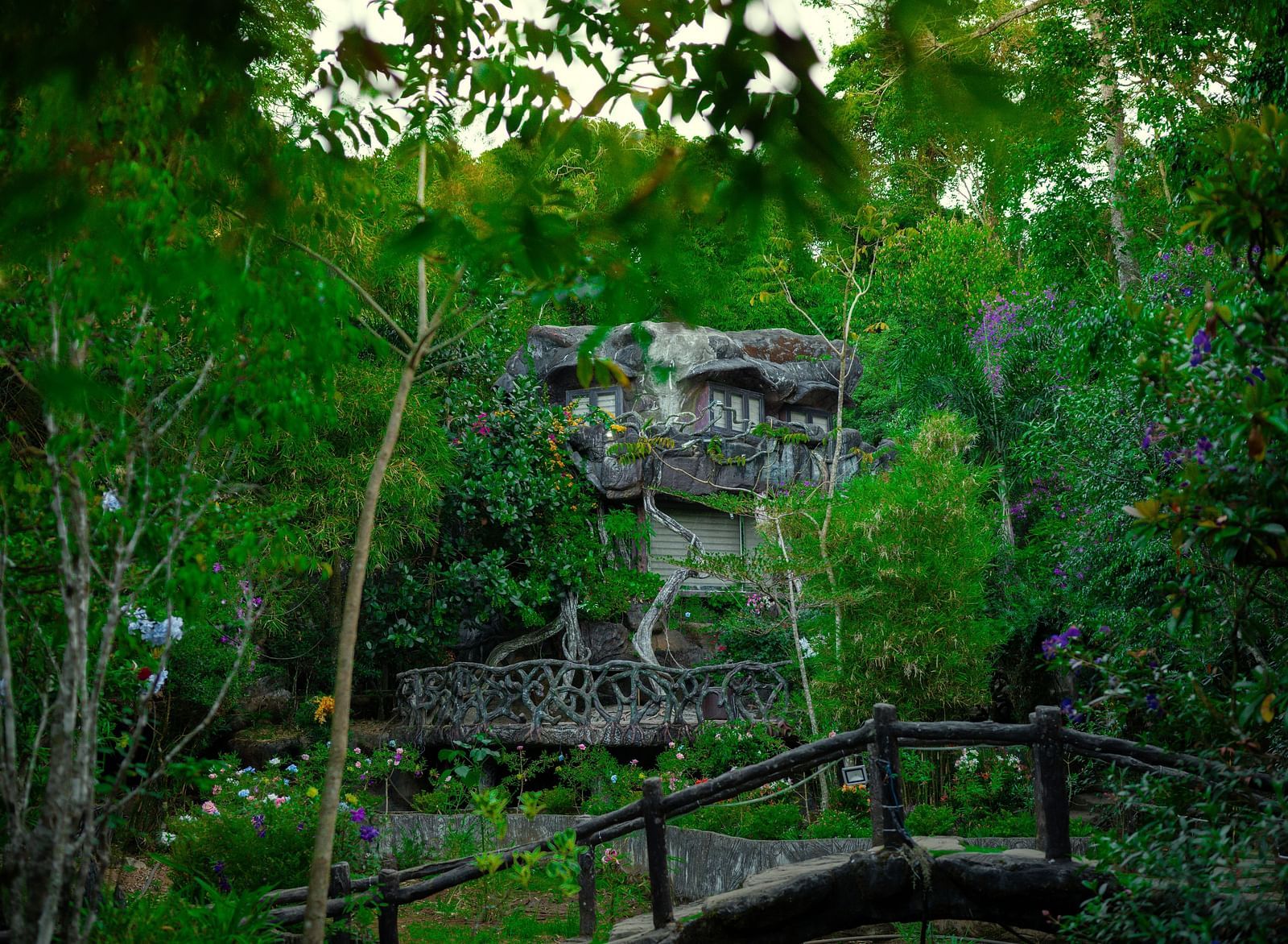 An image of a facade set amidst the forest and there's also a bamboo bridge  in front of the facade - Parakkat hotel & resorts