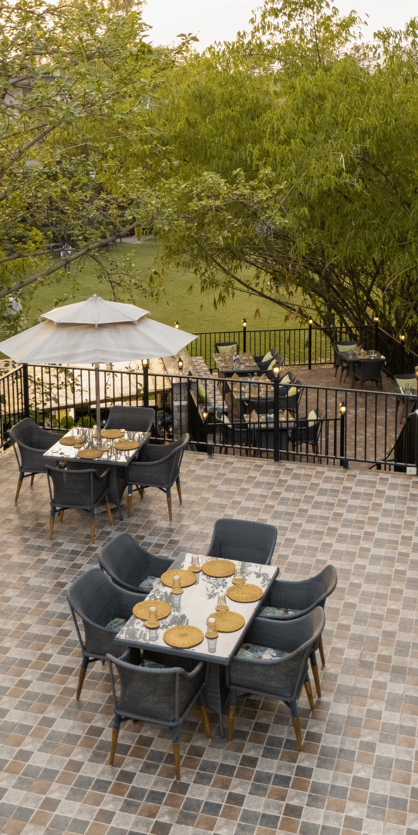 utdoor restaurant patio with multiple tables and chairs under umbrellas, surrounded by lush greenery at The Golden Tusk, Jim Corbett