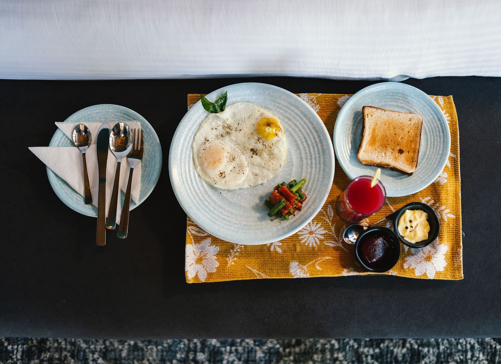 A top view of three plates at BluSalzz Villas - The Green Roof, Bhimtal, featuring toast, an omelette with vegetables, and cutlery alongside jam, butter, and a lit candle.