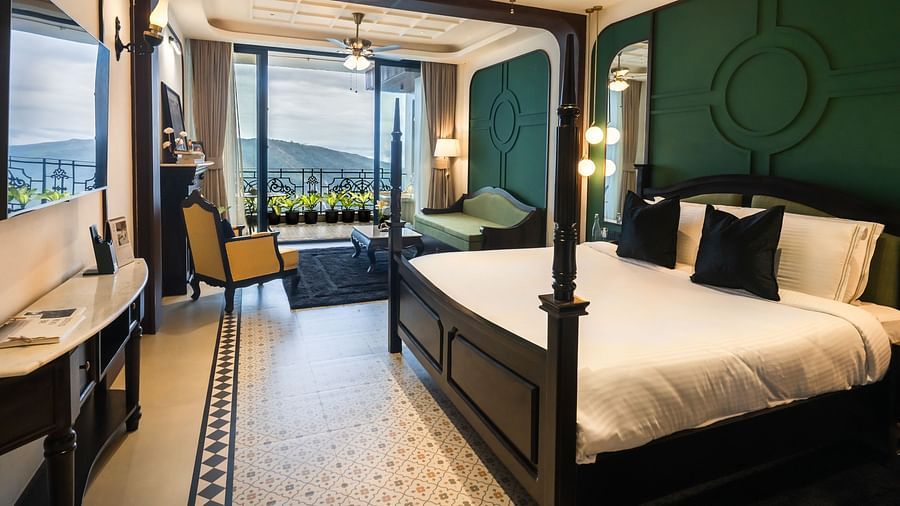 An image of a bedroom with king size bed, flat TV screen, chair, sofa, and a view of the balcony - Polo Orchid Resort, Cherrapunjee - Best Resorts Meghalaya
