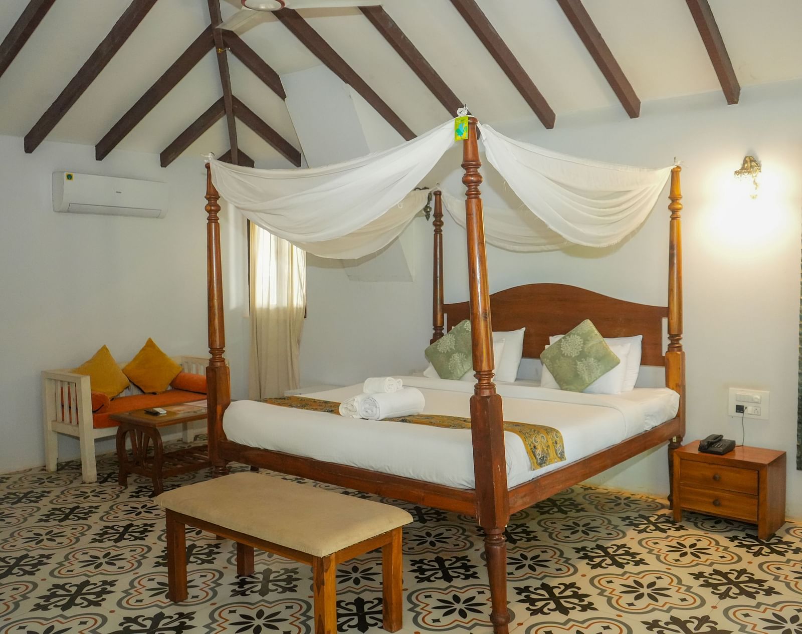 Bright room featuring a wooden four-poster bed with yellow cushions and detailed tiled flooring at De Soul Santé, Morjim.