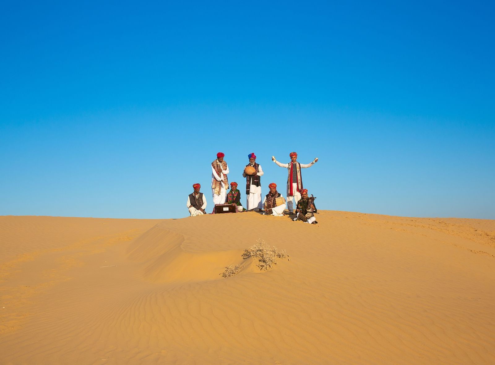  A cultural scene unfolds on a desert dune, with individuals dressed in traditional attire, bringing life and color to the sandy environment.
