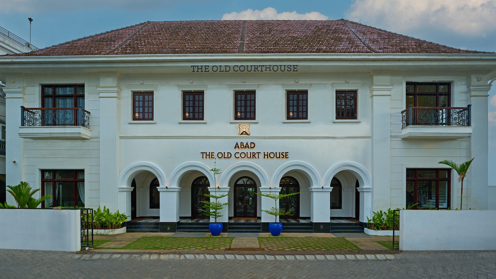 A colonial-style white building with a symmetrical facade, arched entryway, and a sign reading The Old Court House above the entrance