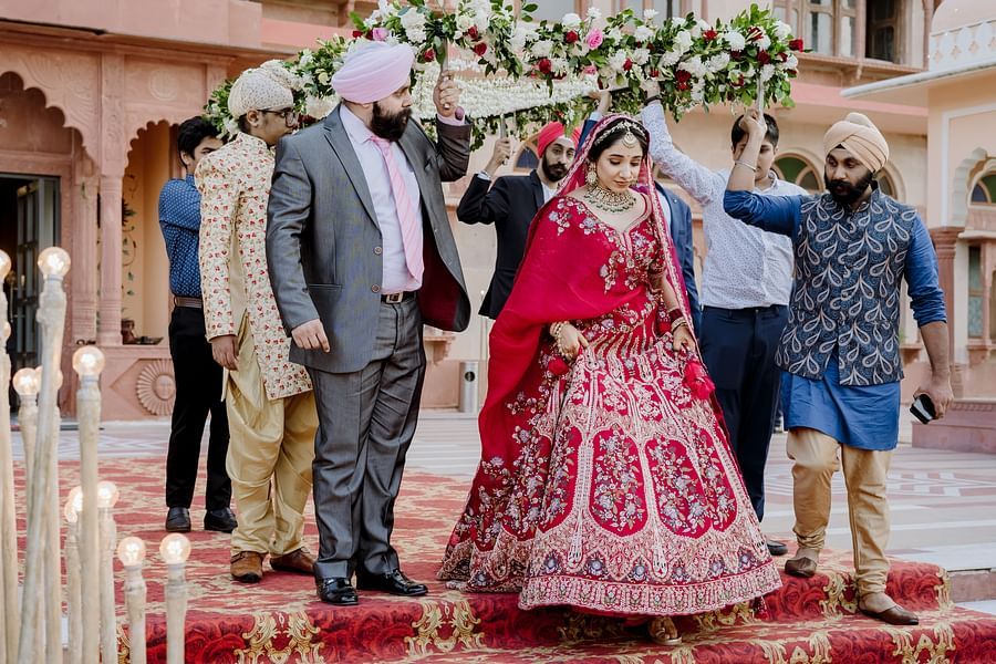 A bride in lehenga is walking down a carpeted path, holding onto a floral canopy carried by several men - Umaid Palace - Best Luxury Heritage Resort Near Jaipur
