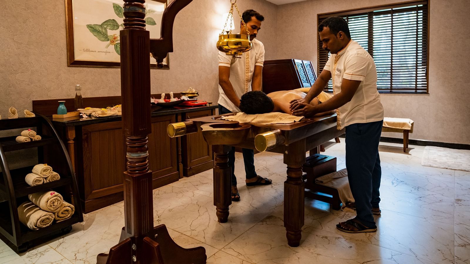Two masseurs performing Abhyanga on a guests who is sleeping face down on a massage table - Gamyam Resort