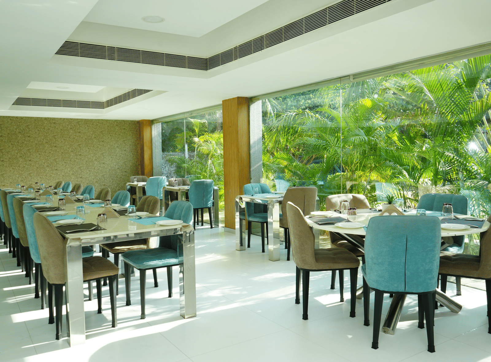 Indoor dining area with elegant table arrangements and large windows showcasing green coconut trees - Grande Bay Resort & Spa, Mamallapuram