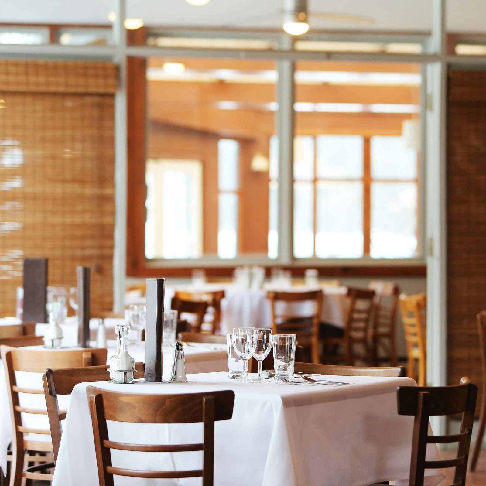 A dining room with wooden tables set with white tablecloths and chairs.
