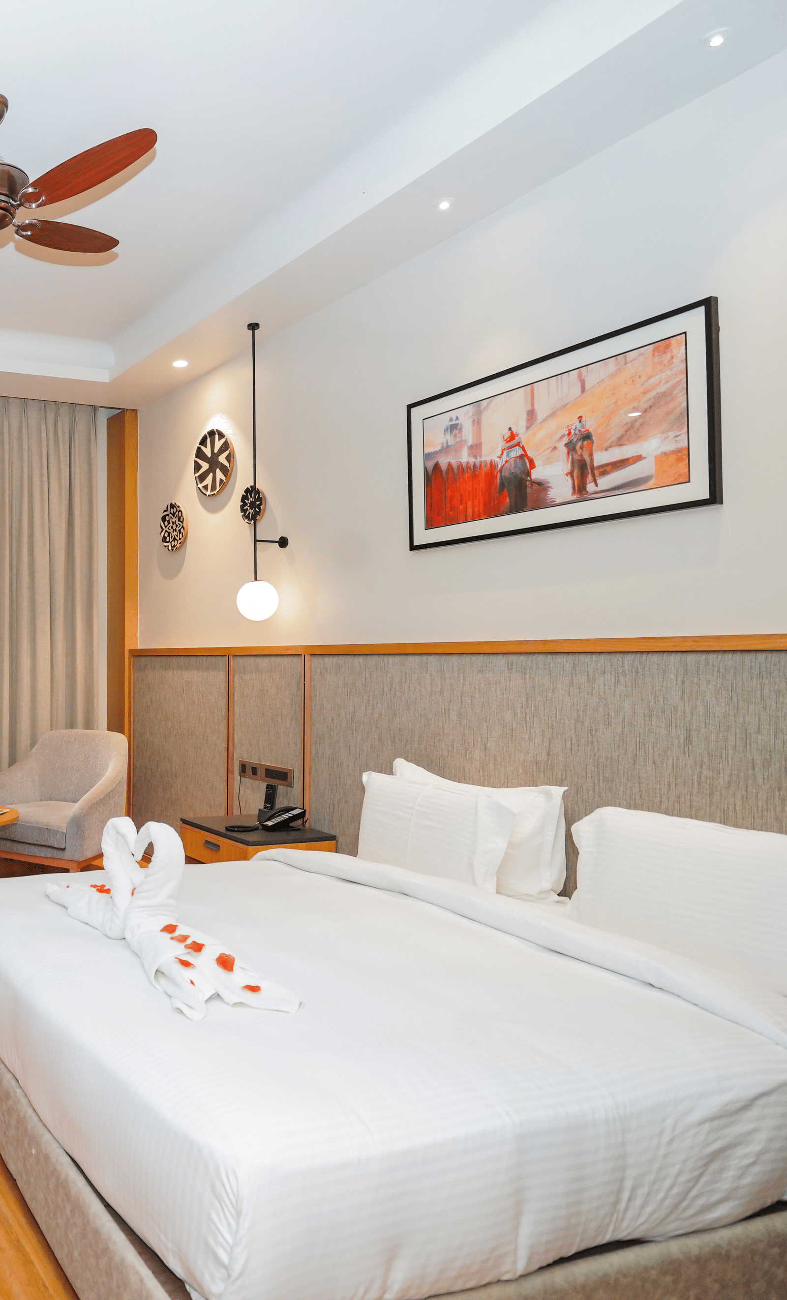 A clean and modern hotel room with a large bed, a TV, and a picture above the bed. The room has wooden floors and a ceiling fan.