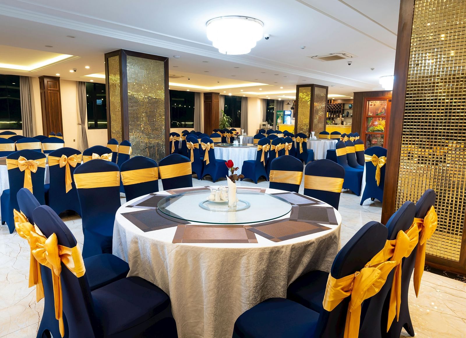 Elegant event space featuring round tables with floral arrangements, blue and gold decorated chairs, and decorative columns
