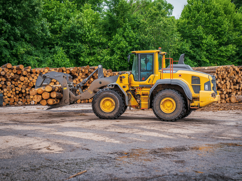 Loader vehicle transporting logs in a timber processing yard.