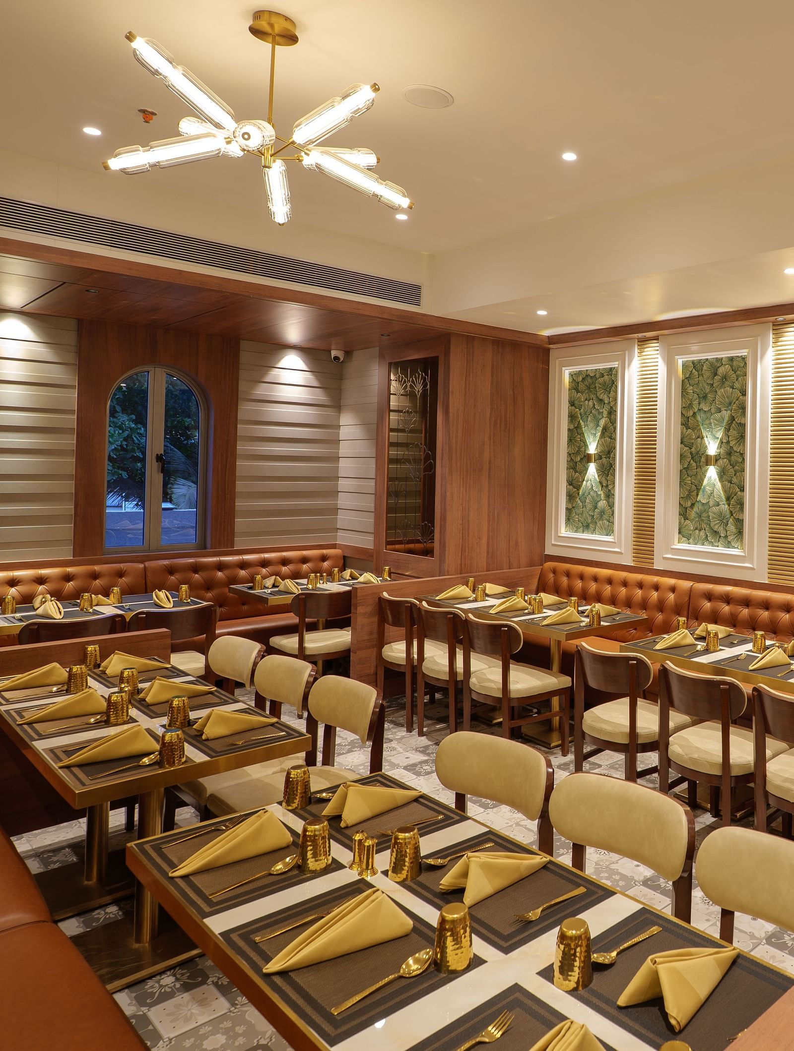 A well-lit restaurant displays set tables, wooden chairs, warm lighting, and decoration on the walls - Melior Inn