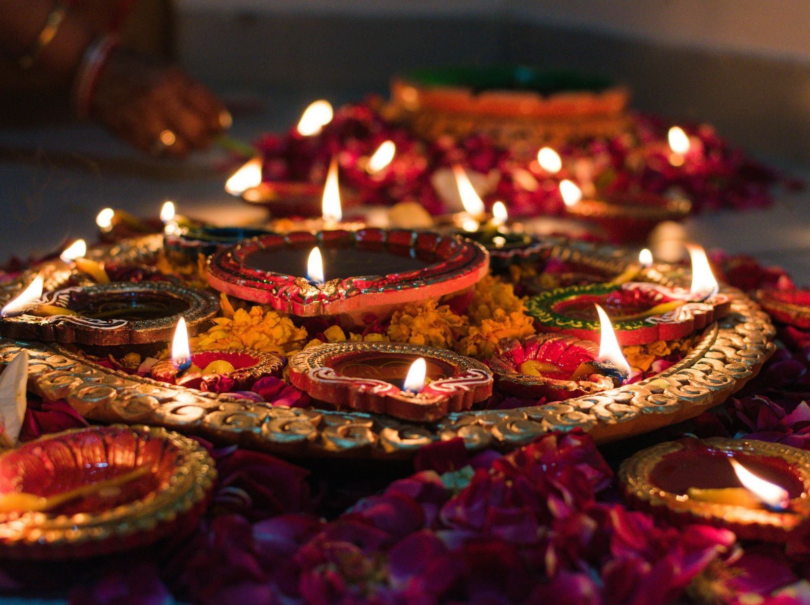Small oil lamps lit during a hindu festival and the lamps are surrounded with flowers and loose petals.