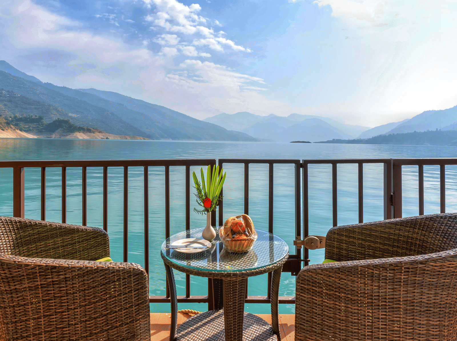A closeup of two chairs surrounding a coffee table with the expansive views of the lake surrounded with mountain ranges at Le ROI Floating Huts & Eco Rooms.