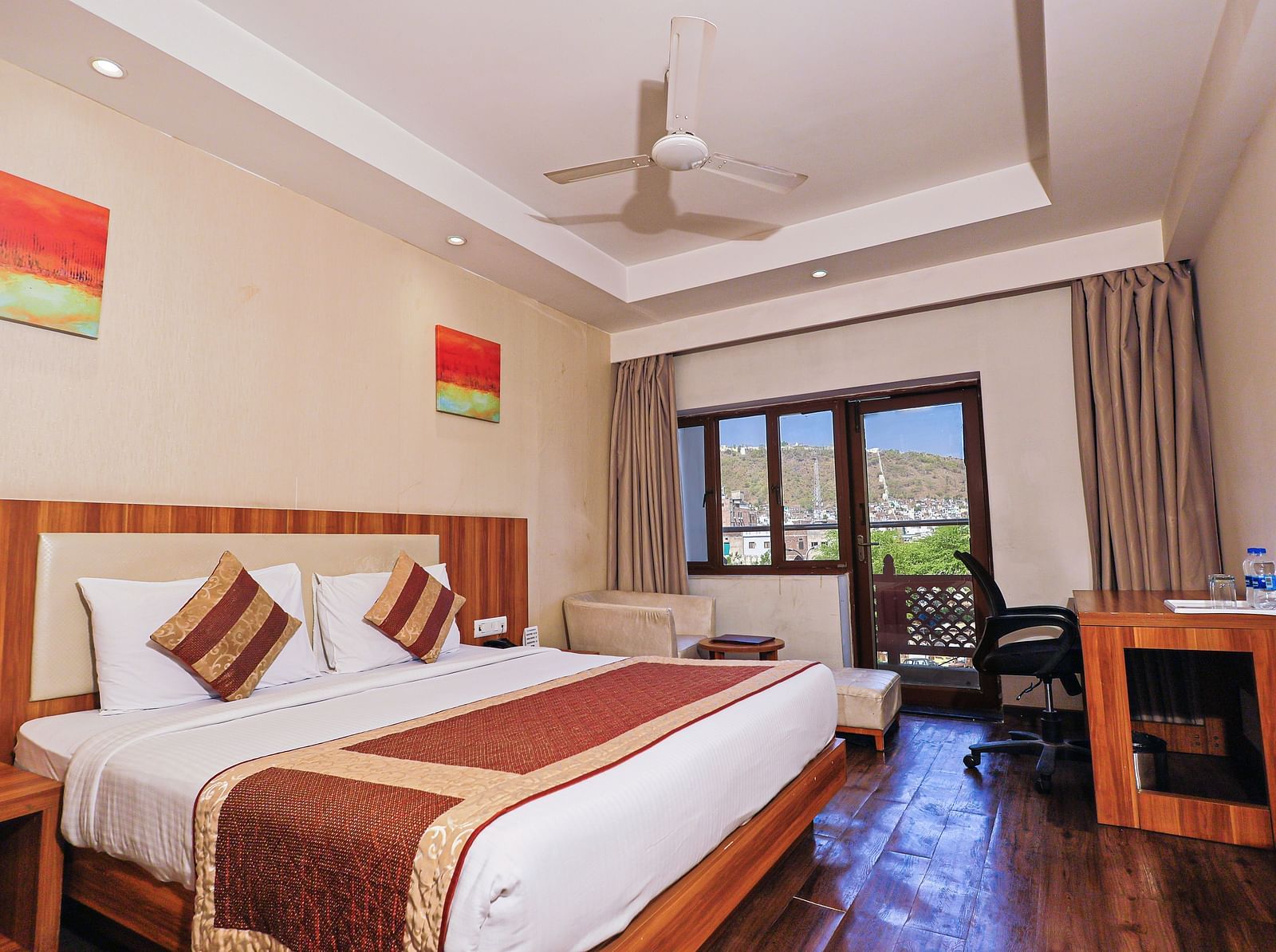 A low angle view of the bedroom with comfy bed and balcony, table and fan at Le Roi Udaipur