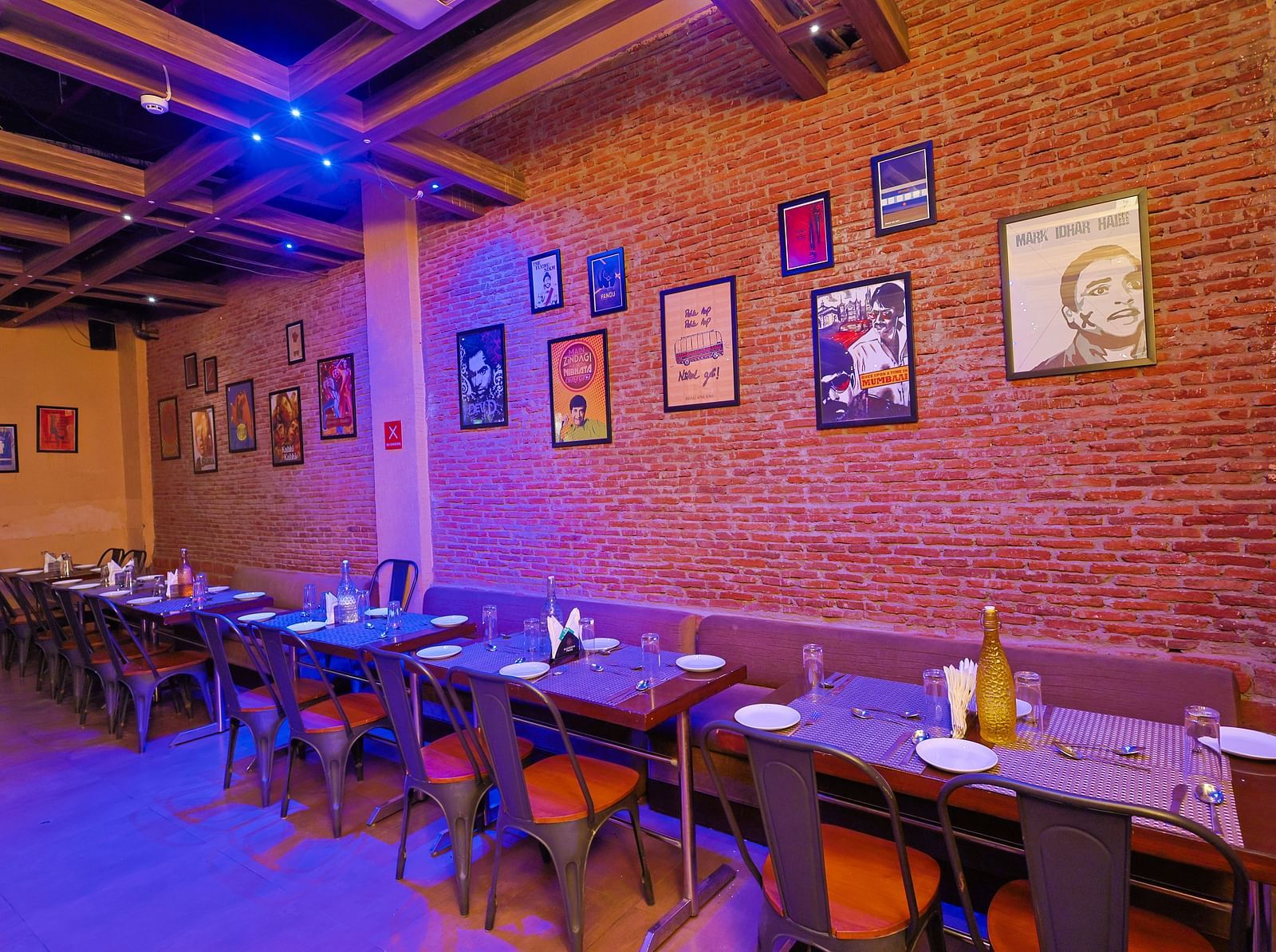 A restaurant with blue lighting to enhance the atmosphere, tables and seating arranged elegantly, and walls adorned with numerous posters