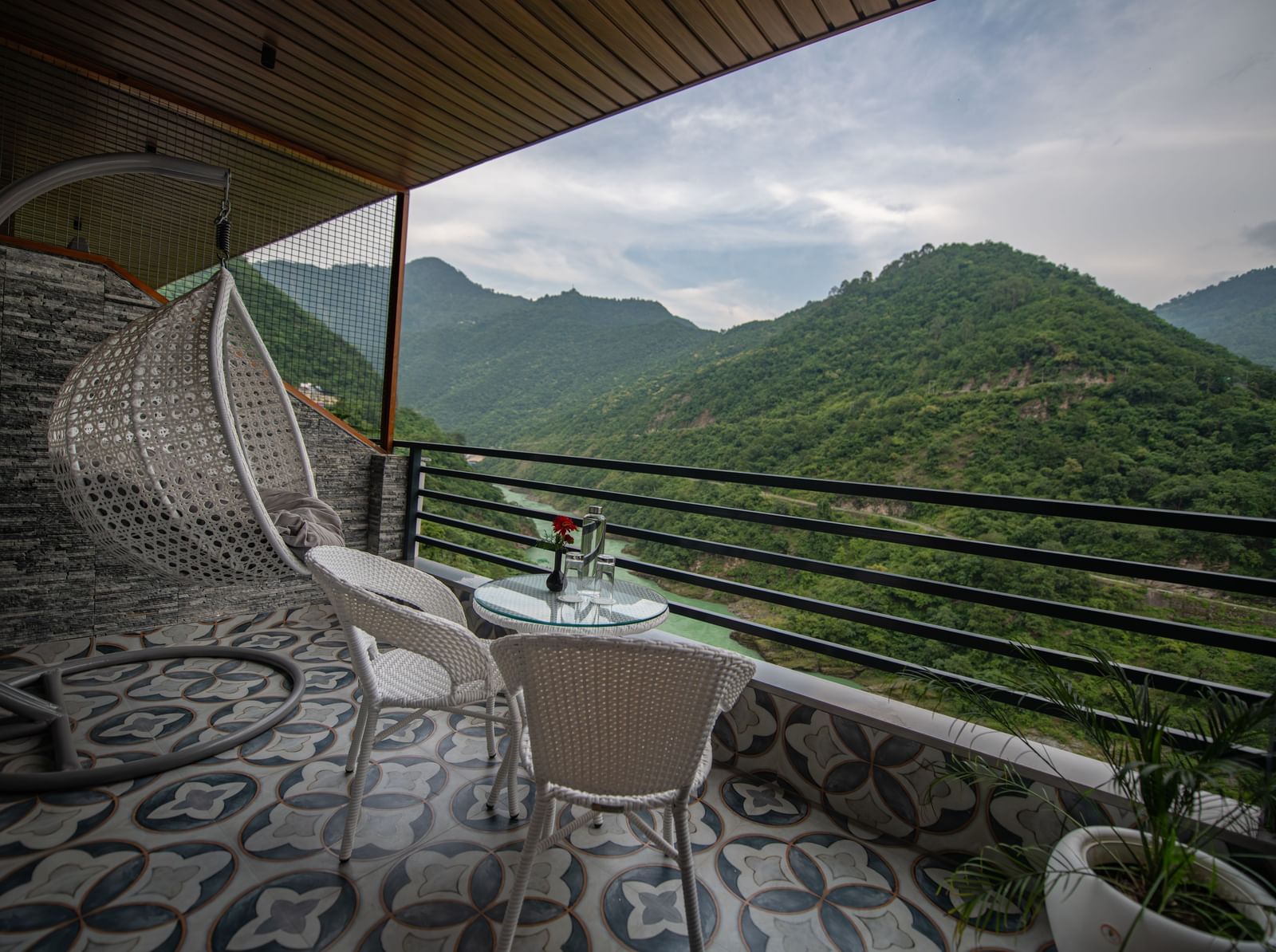Balcony at The Tattva Devaprayag with two white chairs and a table overlooking the mountains and flowing river.