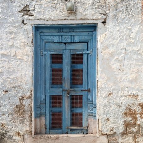 Old blue door and window on a weathered white wall.