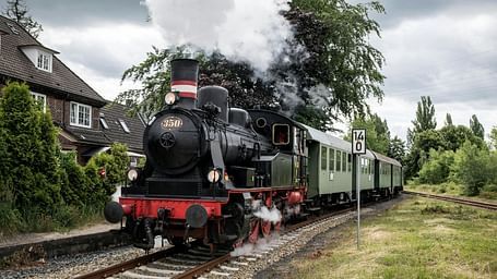 A vintage steam train passing by houses under a cloudy sky.