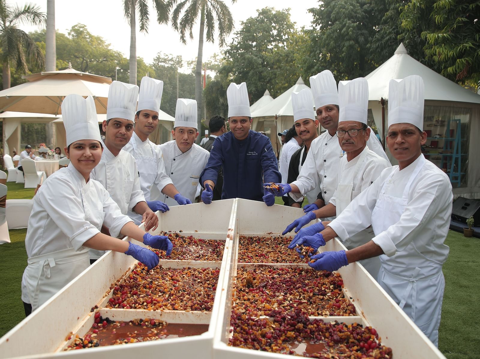 Image of people posing for a photo while preparing a cake in the open, spacious garden at The Claridges New Delhi