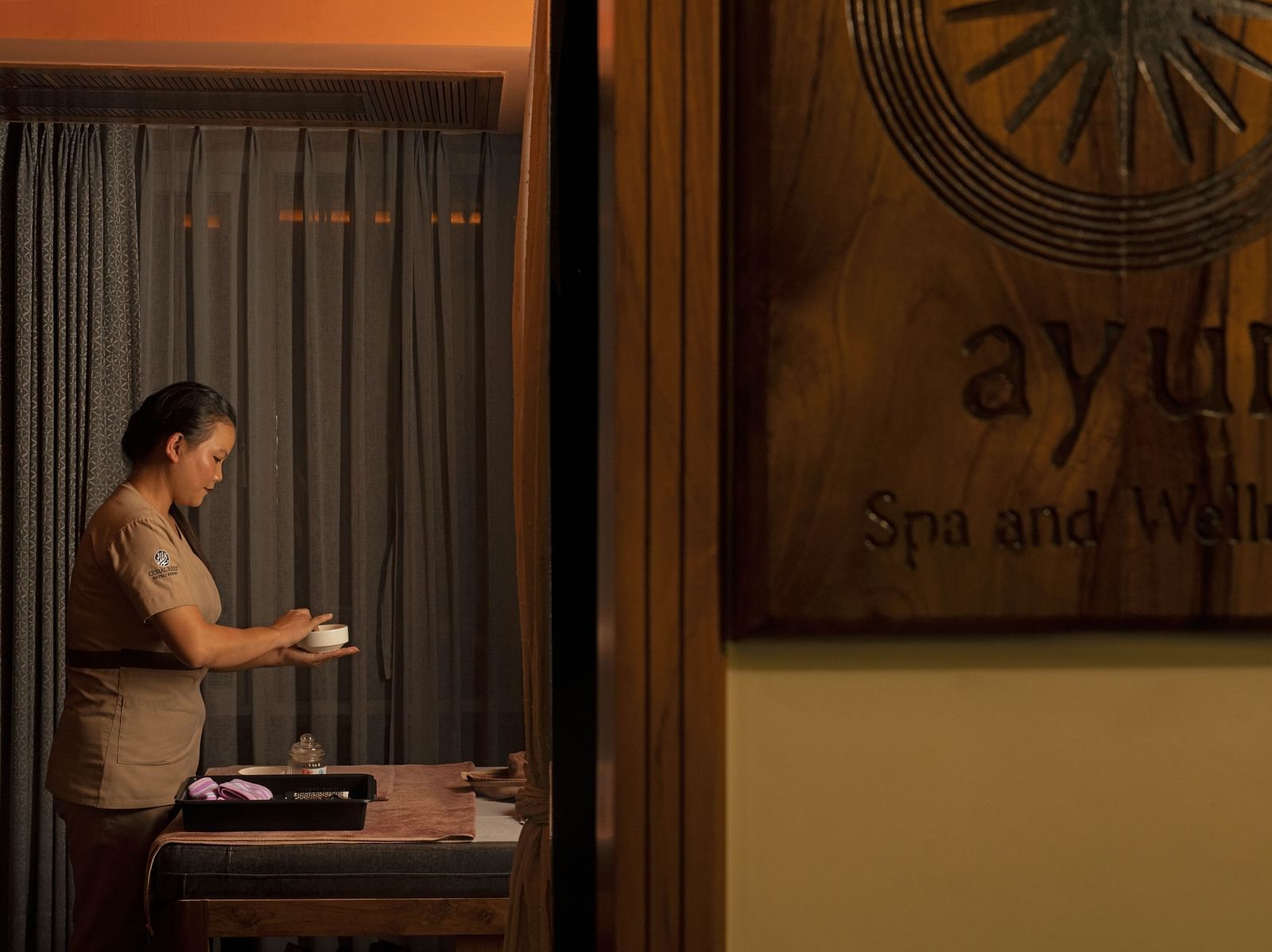 Image of Ayur Spa at Coral Reef Hotel and Spa in Port Blair featuring a masseuse preparing essentials for spa holding a little bowl