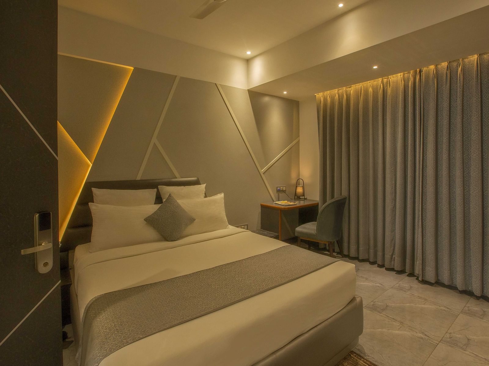 Image of well lit Coral Premium Room at Coral Reef Hotel and Spa in Port Blair featuring a plush bed and a work desk and chair next to it near the window
