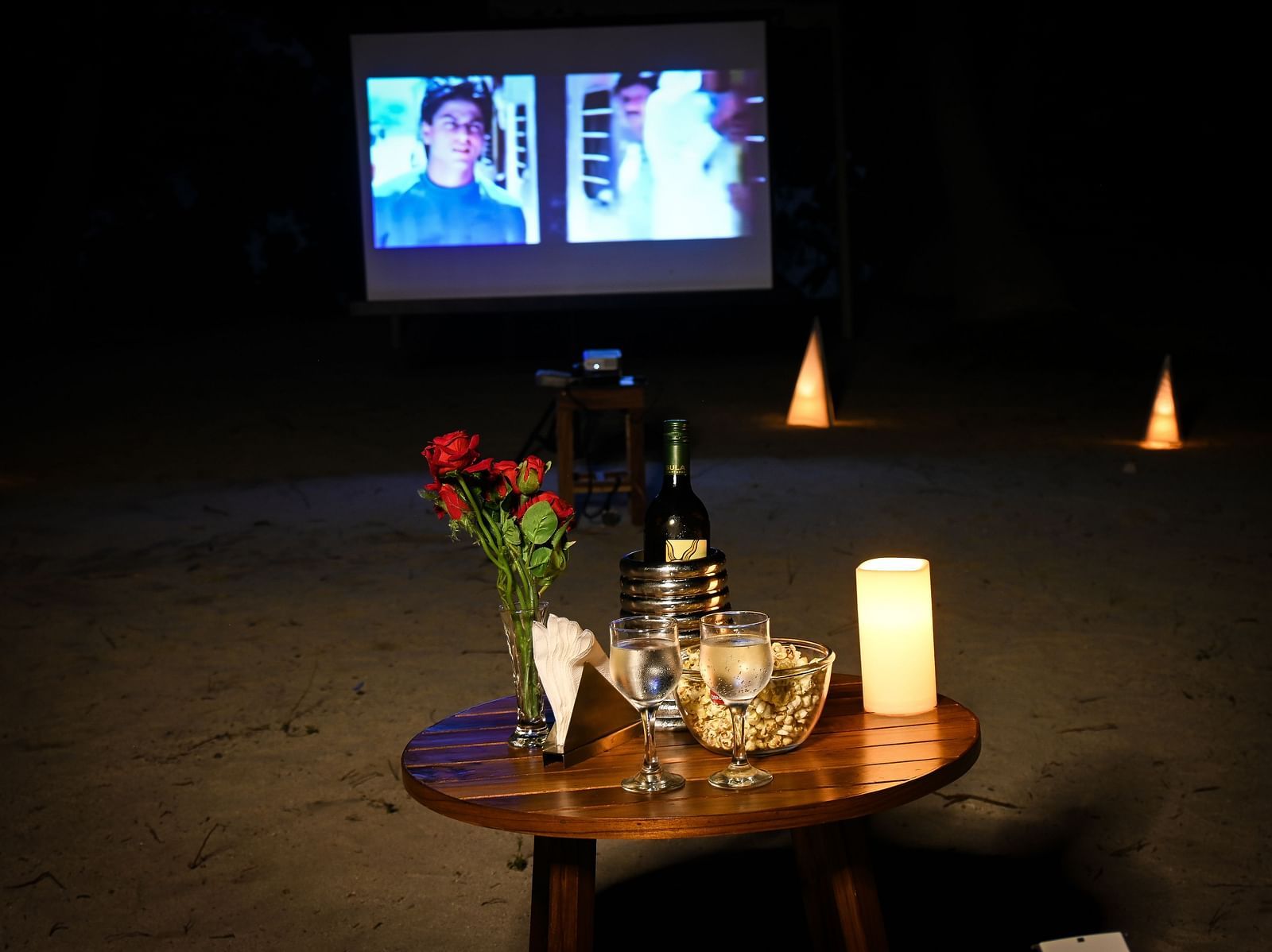 A small table with glasses wine rose on top and a movie playing in the white screen in the background - Coral Reef Resort & Spa, Havelock