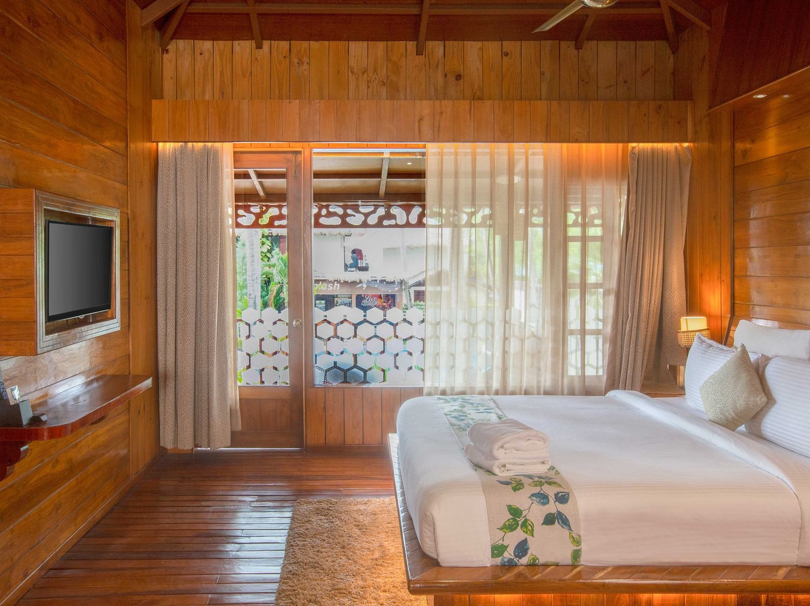 Image of Coral Turquoise at Coral Reef Resort and Spa in Havelock featuring a plush bed with a TV mounted on the wall in front of it and the doorway to the balcony