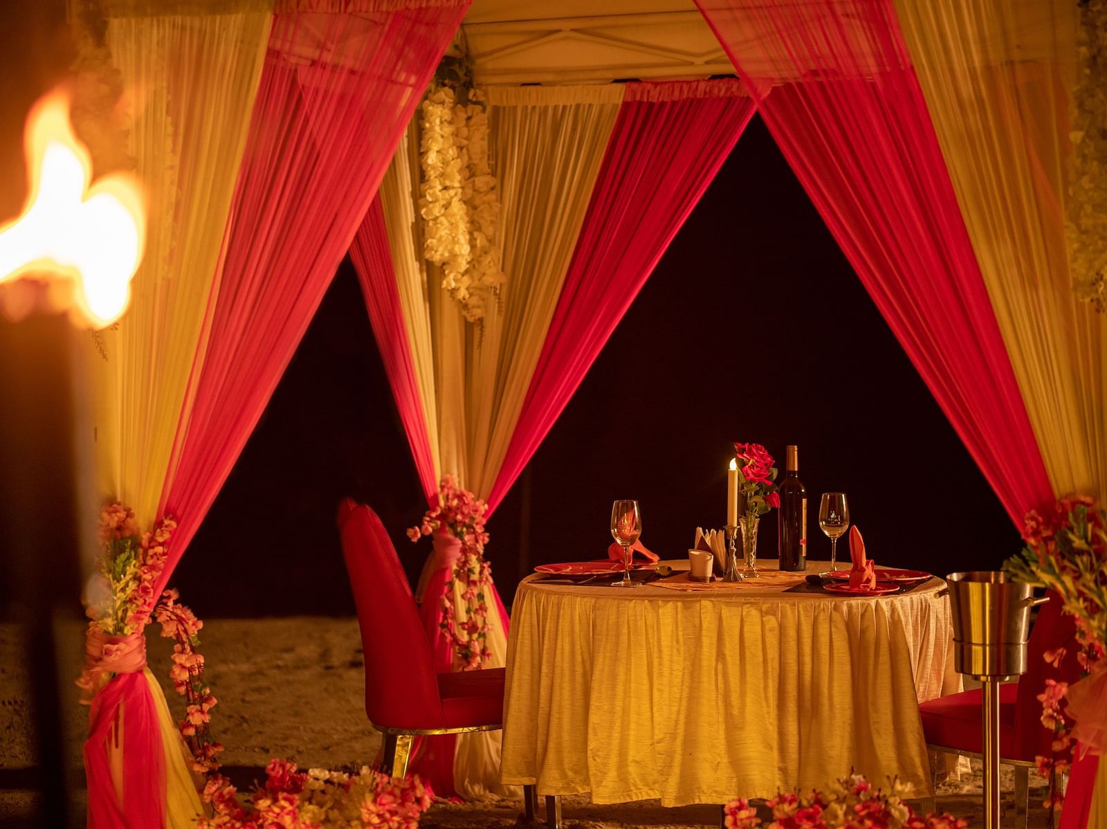 Inside view of a beach canopy with a dining table, lit by torches and surrounded by candles - Coral Reef Resort & Spa, Havelock