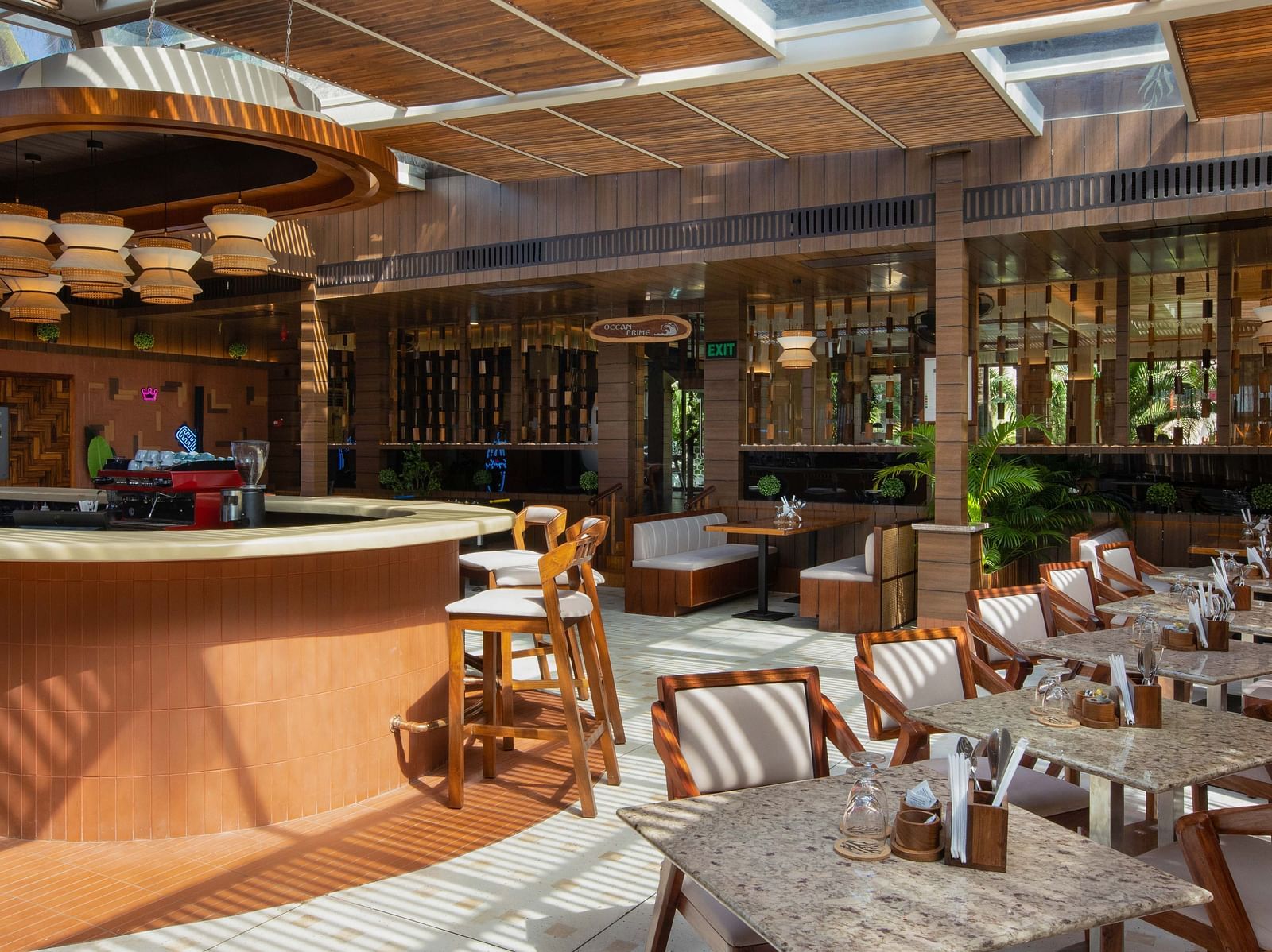 5th Bistro Cafe featuring a beautifully designed interior and dining area with wooden tables and chairs, suspended lighting fixtures, and tropical greenery. The space has a relaxed, elegant atmosphere - Coral Reef Resort & Spa, Havelock