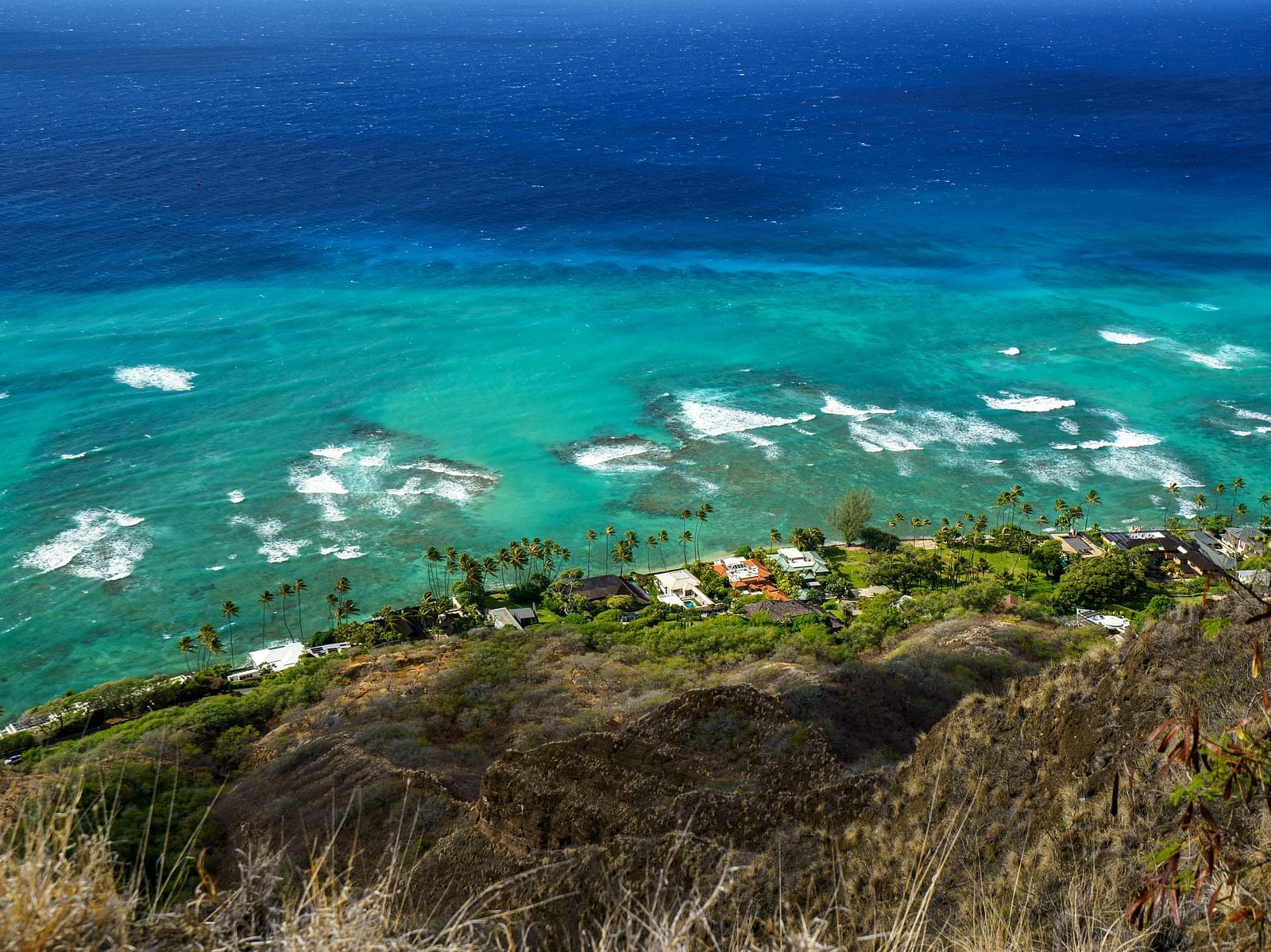 A sky view of houses placed on a cliff of a mountain beside a clear blue sea