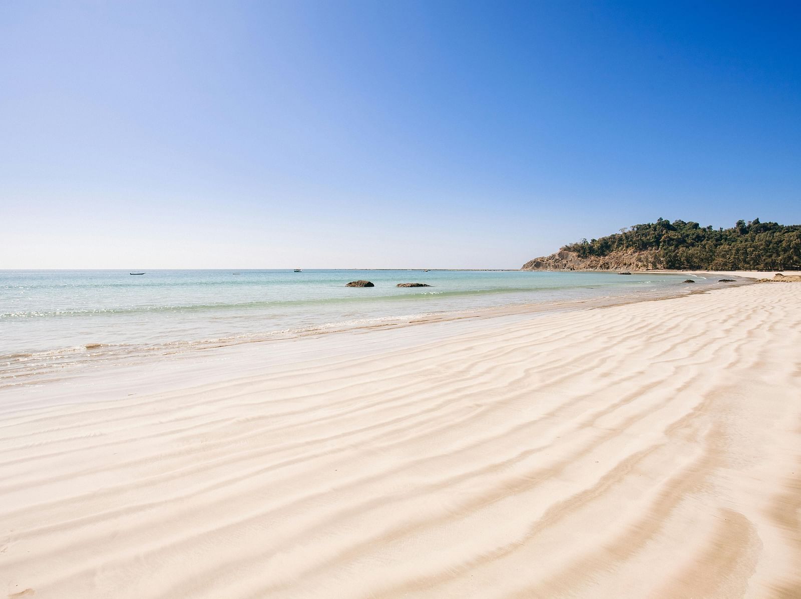 A tranquil beach with soft white sand, gentle waves and a clear blue sky