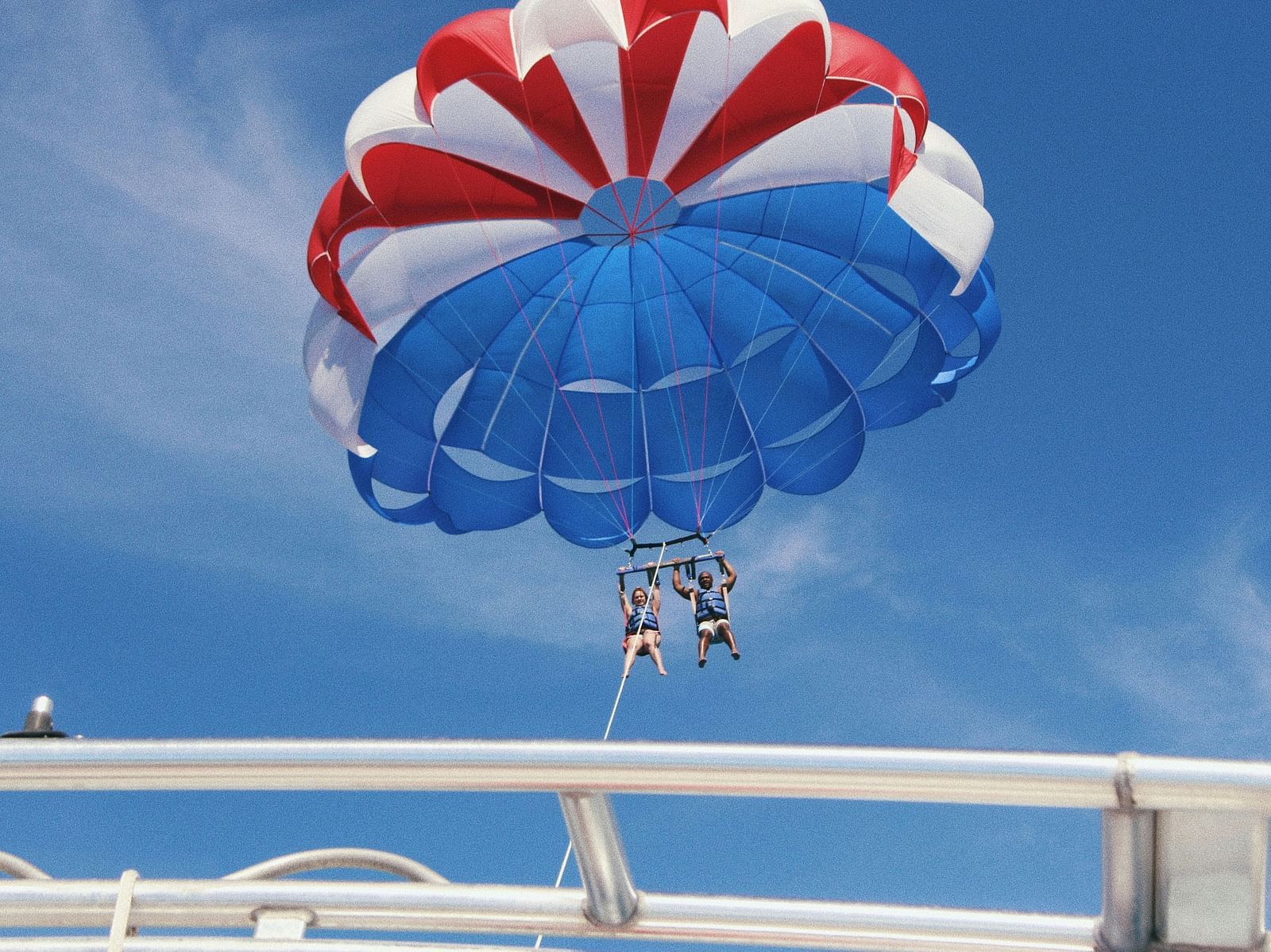 A view from inside a boat of two people Parasailing with a tether to the boat. 