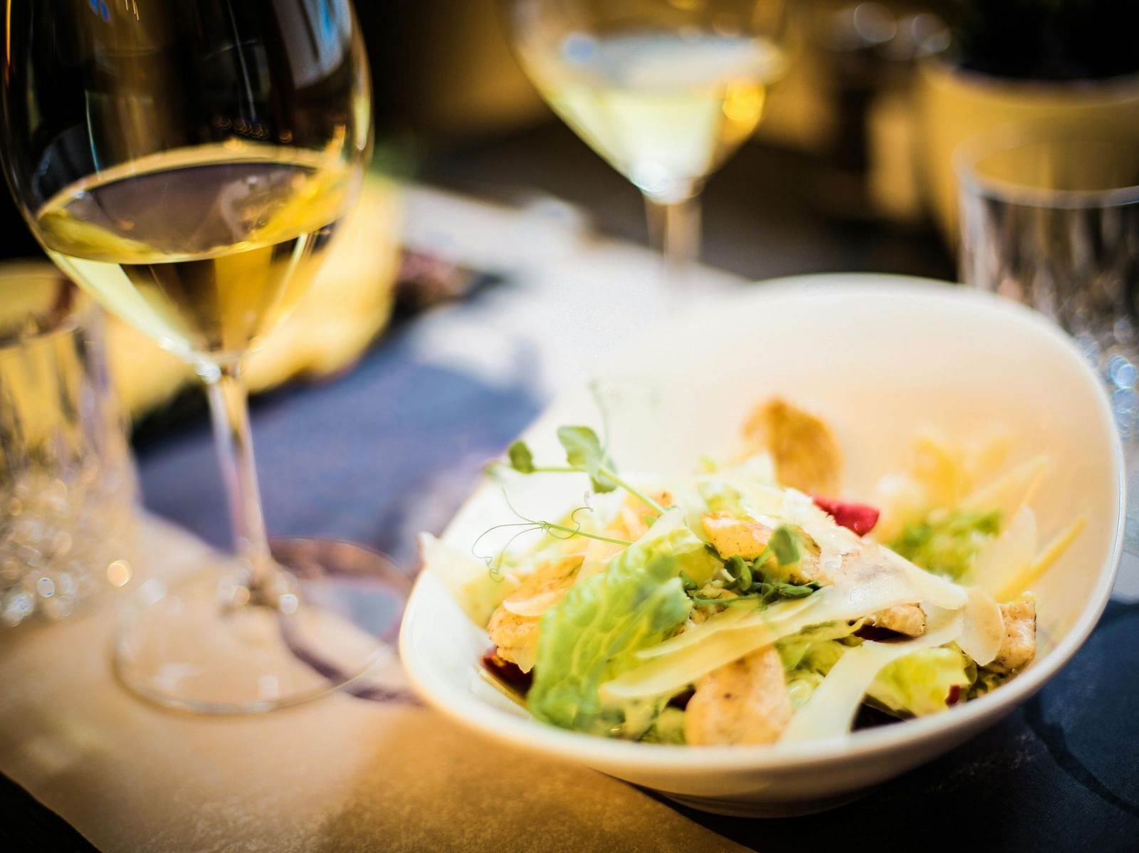 A fine dining experience featuring a bowl of salad with a glass of white wine in a softly lit ambience