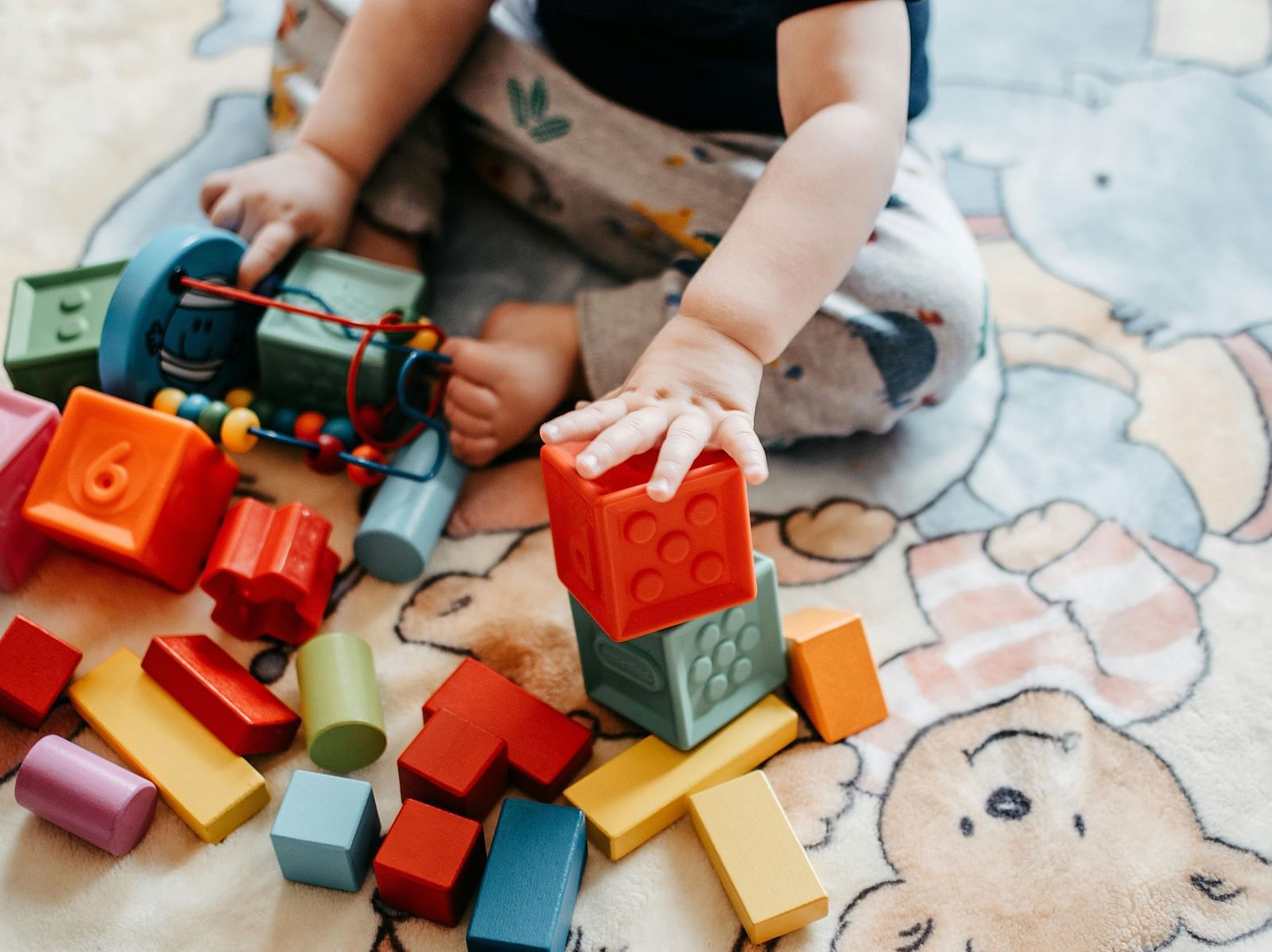 A toddler playing with colorful building blocks on a playful bear-themed mat