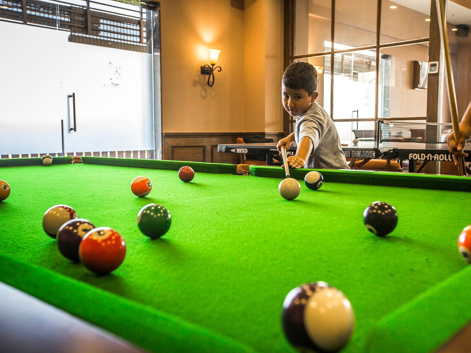 an image of a kid playing pool on the pool board - Rhythm Lonavala
