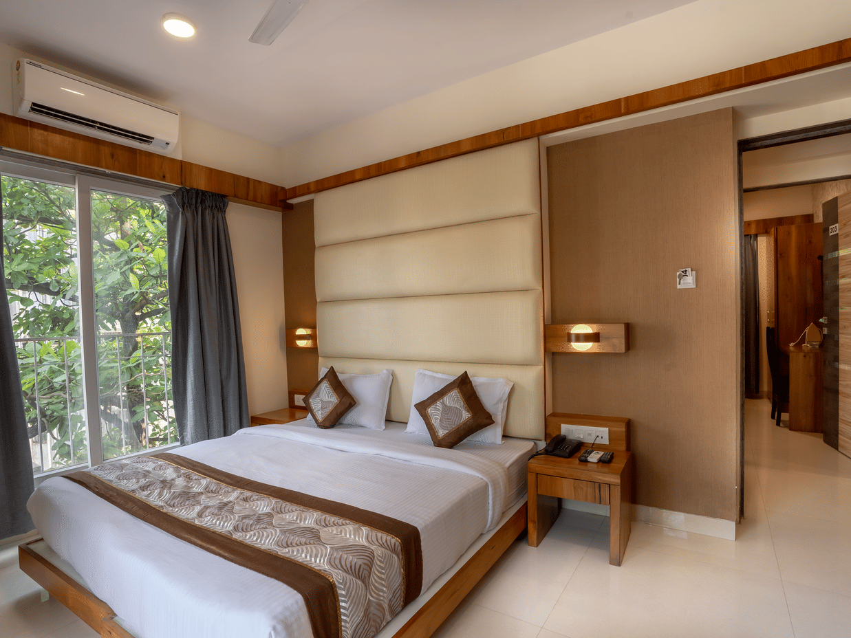 Bedroom featuring a plush bed next to the glass door to the balcony with an air-conditioner over it at Home2 Suites & Service Apartments for a pleasant stay near Mumbai Airport