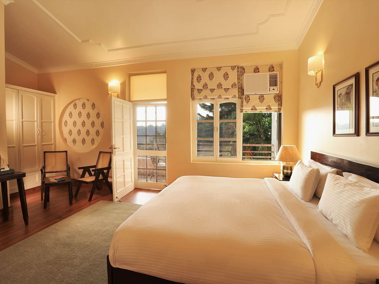 An image of a Super Deluxe Room featuring a double size bed, two chairs, a table where coffee maker is kept, and an open door from where sunlight is flooding the room - Lamrin Boutique Cottages Rishikesh
