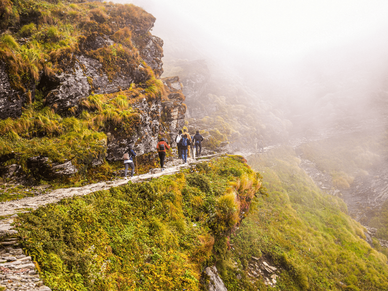 A group of people walking on a rocky hiking trail leading to the misty valleys of a mountain range.