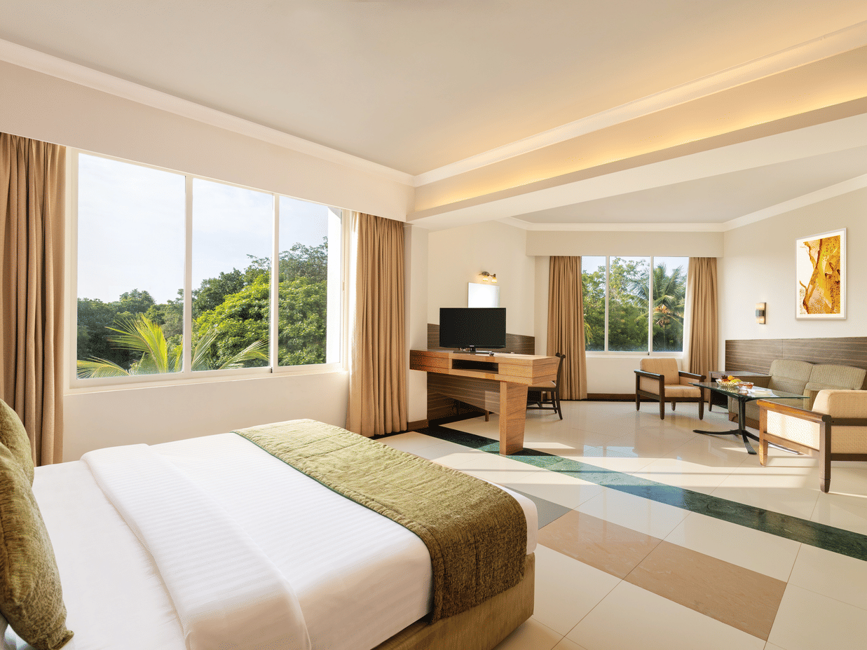 A double bed and a living area opposite it with a tv and sofas inside the Deluxe Room at Sangam Hotel, Thanjavur - Thanjavur Hotel Rooms