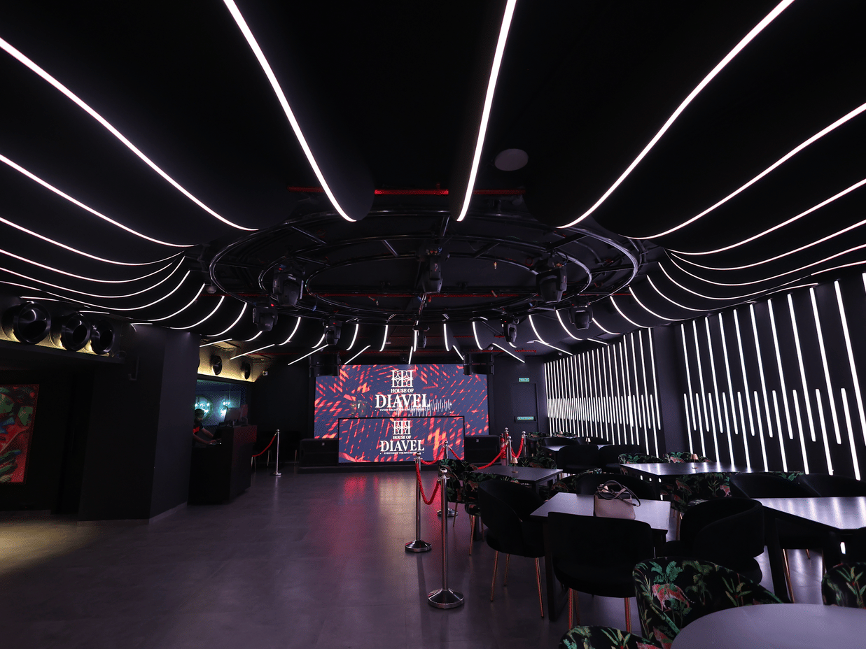 Dark club interior at The Beatle Hotel, Powai. Dramatic ceiling and wall lighting with white LED strips, overlooking tables and a screen.