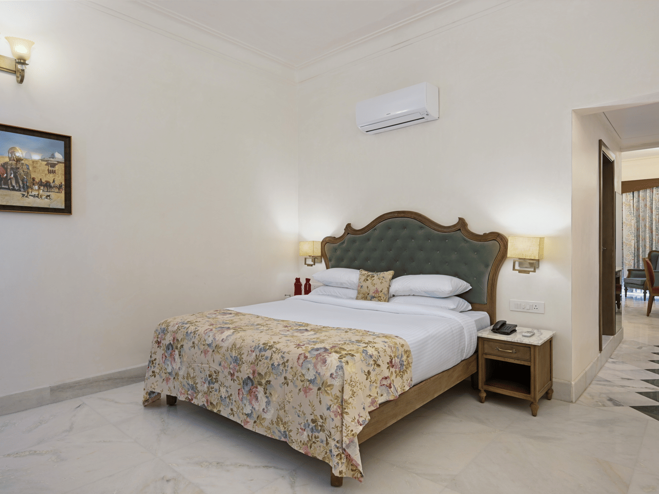 Interior view of the Family Plunge Pool Suite in Udaipur at Fateh Vilas, featuring a king size bed, an air conditioner overhead and lamps on both sides over the nightstands
