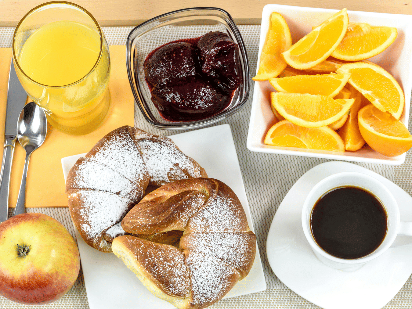 Breakfast spread with croissants, jam, orange slices, coffee, and juice.