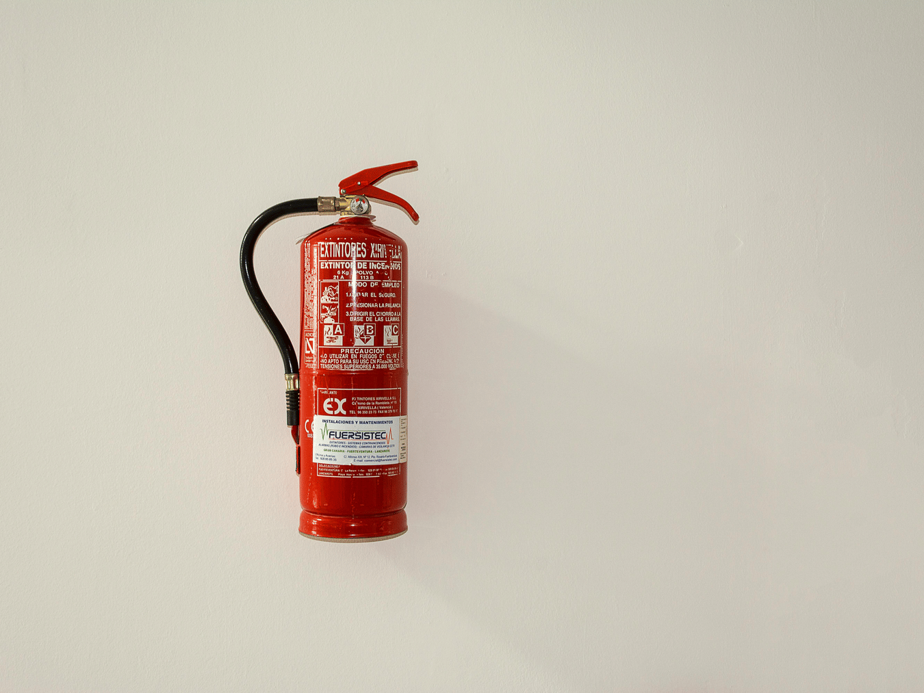 Red fire extinguisher mounted on a clean, light-coloured wall.
