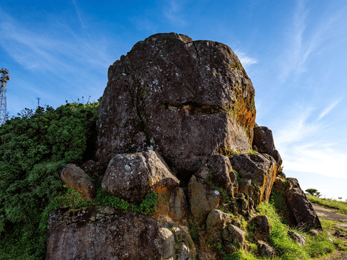 A striking natural rock formation rising above lush greenery under a clear blue sky, offering spectacular views of the surrounding landscape.