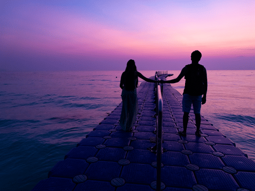 A couple walking during sunrise at Kalapathar Beach while standing on a man-made pier and looking at the sky