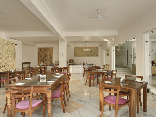 Lobby restaurant at Fateh Safari Resort, Kumbhalgarh featuring tables and chairs and a kitchen counter with plates, cutlery, bowls, jugs, etc.