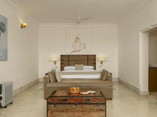 Plunge Pool Suite with Jacuzzi at Fateh Safari Suites, Kumbhalgarh featuring a bed, lamps and bedside tables on either side, a sofa at the centre, and a table where fruits and other foods are kept. 