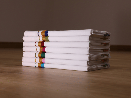 A neat stack of six dhotis with decorative borders on a wooden floor