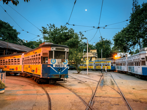 Two traditional Kolkata trams traveling side by side on parallel tracks through the city, showcasing the charm of Kolkata's iconic public transport system.