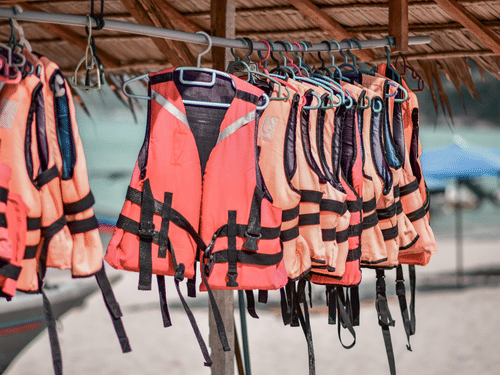 Multiple life jackets hanging on a rack at a beachside water sports centre, ready for visitors participating in water-based adventure activities.